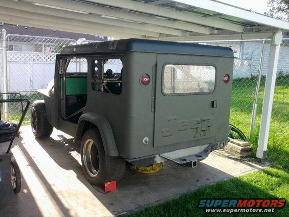 Jeep CJ-8 Scrambler parked under a carport, rear view. It has a hardtop and is painted olive drab