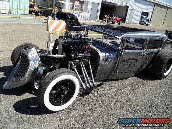 Custom hot rod with exposed engine, chrome grille, and whitewall tires. Text on door reads 'Nickel's Customs'