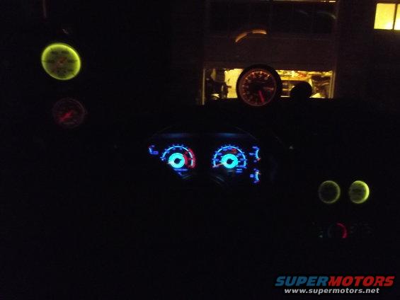 Car dashboard at night with glowing blue and red gauges and two yellow circular gauges