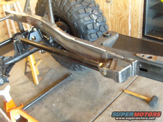 Jeep CJ frame with suspension components and a large off-road tire, supported by jack stands