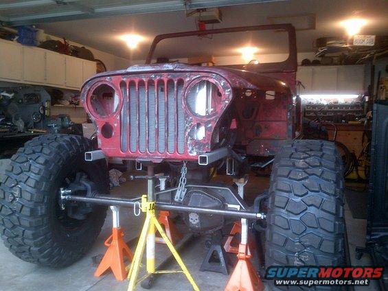 Red Jeep CJ-series body on jack stands, front view with large tires