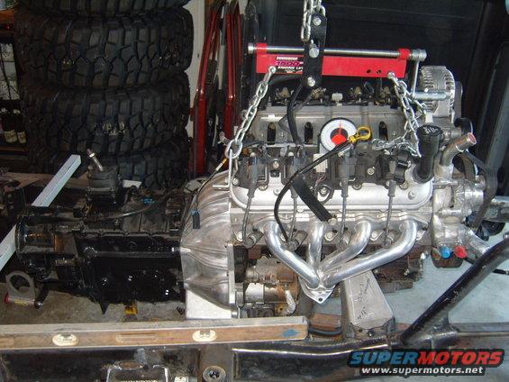 Engine and transmission assembly suspended by a red engine hoist, with exhaust headers attached