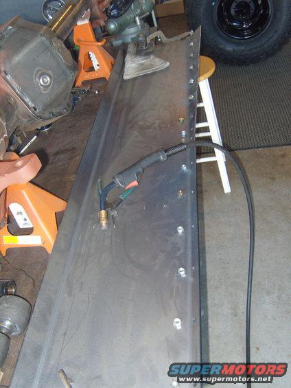 Sheet metal panel with pre-drilled holes and a welding gun, on sawhorses with a tire in the background