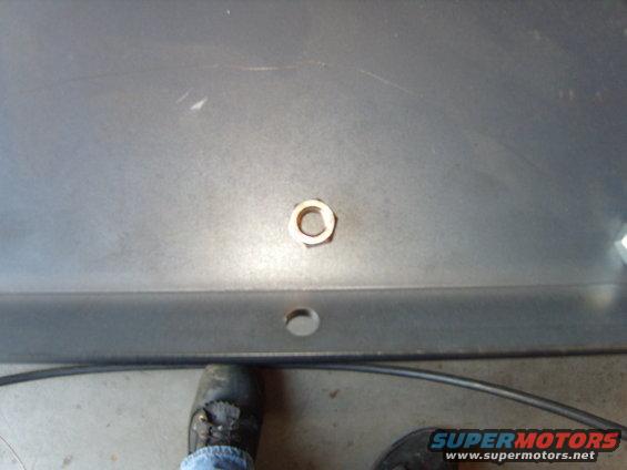 Nut on a gray metal panel with a hole below it