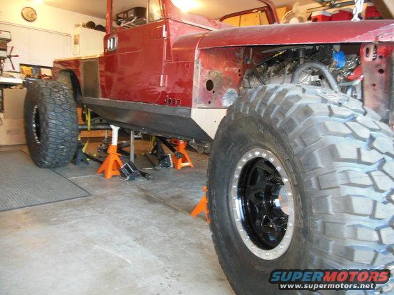 Red Jeep CJ on jack stands, front fender removed, large off-road tires