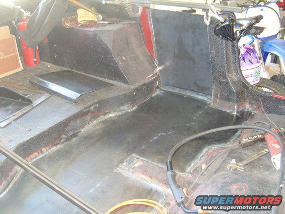 Interior of a Jeep being worked on, showing floor and rear panels. Fire extinguisher and tools are visible