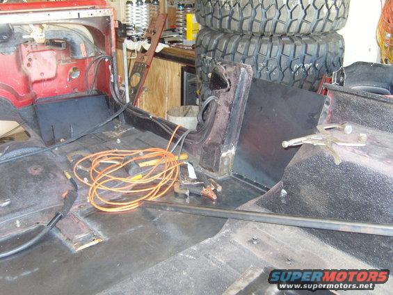 Red Jeep interior with black floor panels, orange welding cables, and stacked tires in background