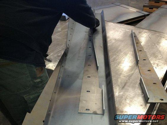 Metal pieces being worked on a workbench, one long piece with holes, another shorter piece