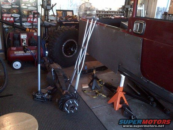Red Jeep CJ-series body side with custom panels, large tire, and workshop equipment