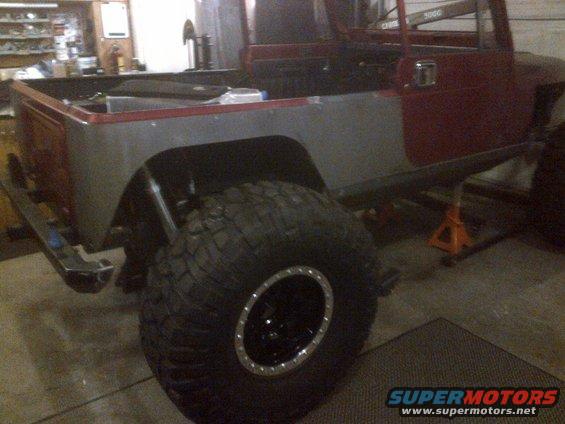 1985 Jeep CJ7 body, red and gray, with large off-road tire, on jack stands in garage