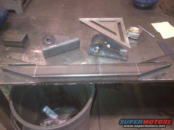 Metal fabrication parts on a workbench with a square and tape measure