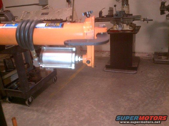 Orange hydraulic cylinder with black hose on a wheeled cart, in a workshop setting