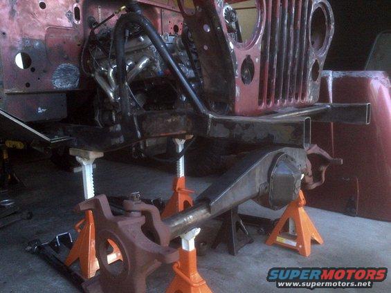 Jeep CJ frame with engine and front axle on jack stands, undergoing restoration