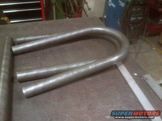 Bent metal tubes on workbench with welding equipment in background