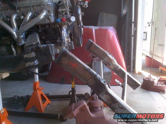 Engine and exhaust headers mounted on jack stands with frame components visible