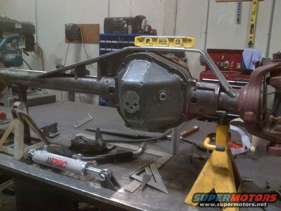 Differential housing with custom skull cover, supported by jack stands, with a steering stabilizer and tools on a workbench