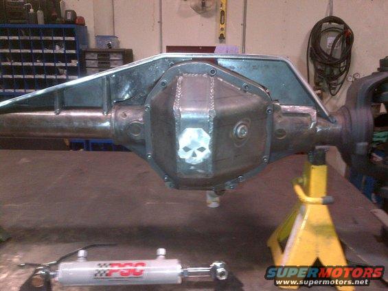 Rear axle differential cover with skull engraving, sitting on a workbench. Hydraulic cylinder in foreground