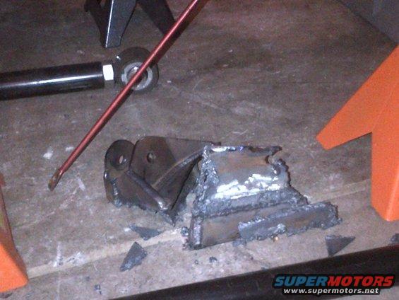 Welded metal bracket with jagged edges on concrete floor, near orange jack stand