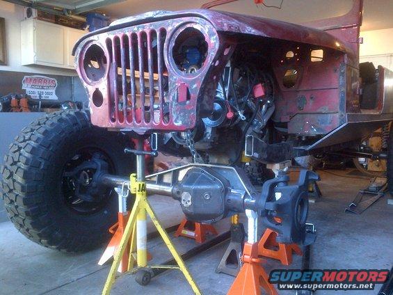 Red Jeep CJ-series front end with grille removed, engine exposed, on jack stands