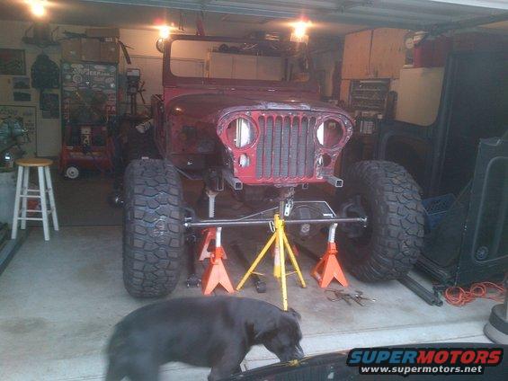 Red Jeep CJ on jack stands, front view, undergoing repairs in a garage