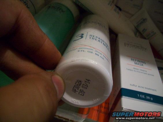 Hand holding a Proactiv Repairing Treatment bottle, with other Proactiv products visible. Expiration date 03/14 stamped on bottle