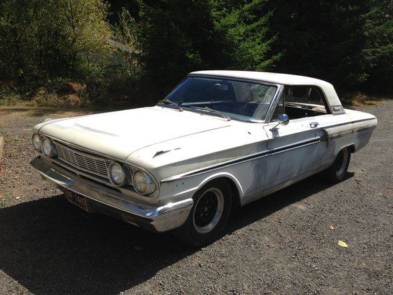 White 1964 Ford Fairlane coupe with primer patches on the body, viewed from the front three-quarter angle