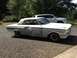 1964 Ford Fairlane - A white 1964 Ford Fairlane coupe, showing primer patches on its body, sits parked outdoors next to a modern SUV.