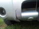 2003 Nissan Frontier - A cracked bumper on a silver truck is visible, with grass and a tire in the foreground.