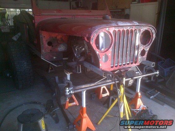 Red 1985 Jeep CJ7 body on jack stands, front view, undergoing restoration