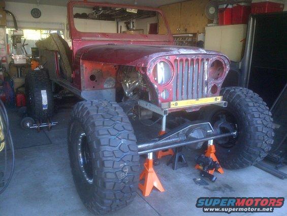 Jeep CJ-series body on jack stands with large off-road tires, undergoing modification in a garage