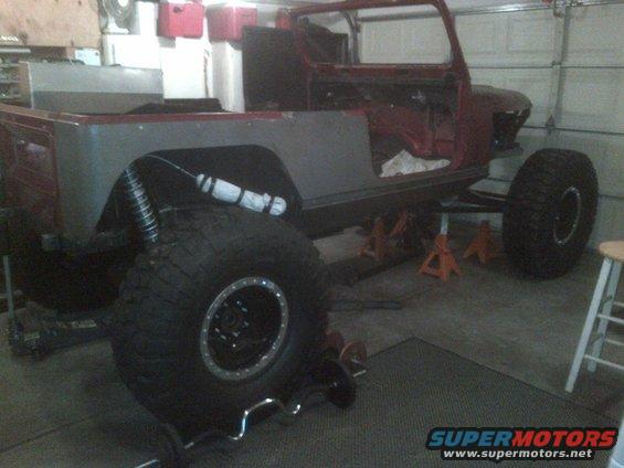 Side view of a red and gray Jeep CJ7 body on jack stands with large tires