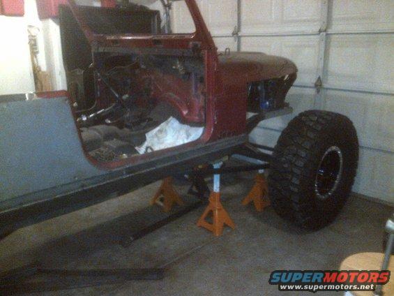 1985 Jeep CJ7 body, red, with large off-road tire, on jack stands in a garage