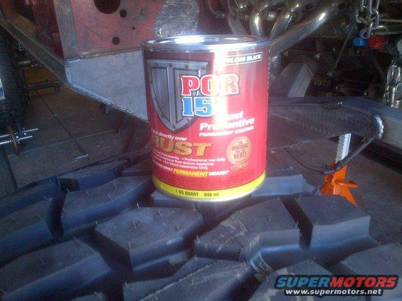 Can of POR-15 rust preventive paint sits on a large tire tread, with vehicle frame and exhaust visible