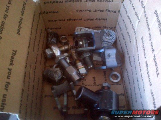 Cardboard box filled with various metal vehicle parts, including bolts, nuts, and what appears to be a differential component