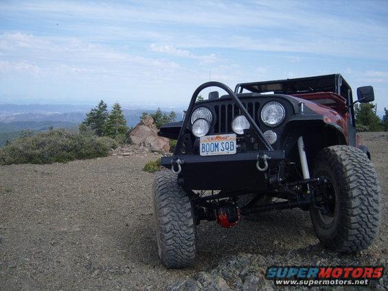 1985 Jeep CJ7 with custom front bumper and off-road tires parked on a rocky overlook