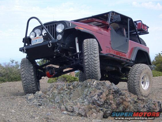 Red Jeep CJ-series off-roading over rocks, lifted with large tires and a roll cage