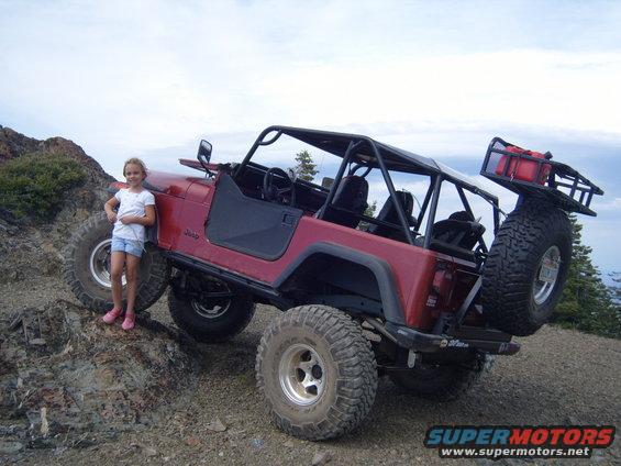 Red Jeep CJ-series off-road vehicle with a roll cage and spare tire on the back, parked on a rocky incline