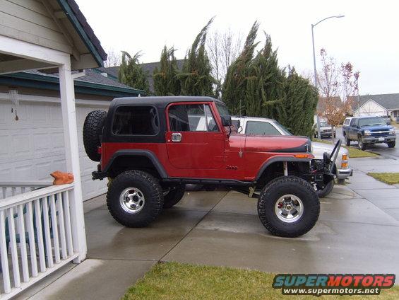 1985 Jeep CJ7 parked in driveway, black hardtop, spare tire on rear. Another Jeep and a pickup truck are visible behind it