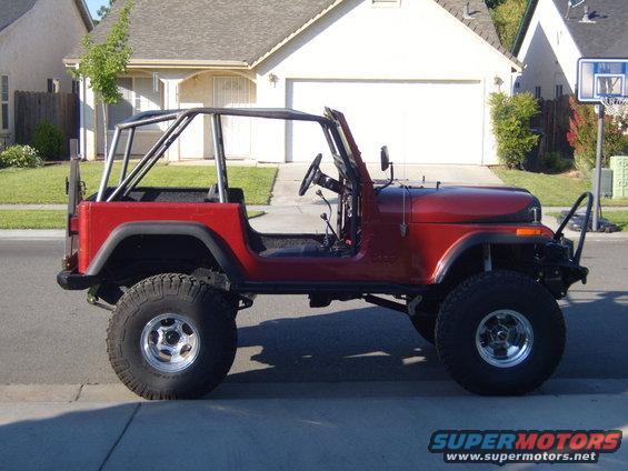 Red Jeep CJ7 with roll cage, aftermarket wheels, and off-road tires, viewed from the side
