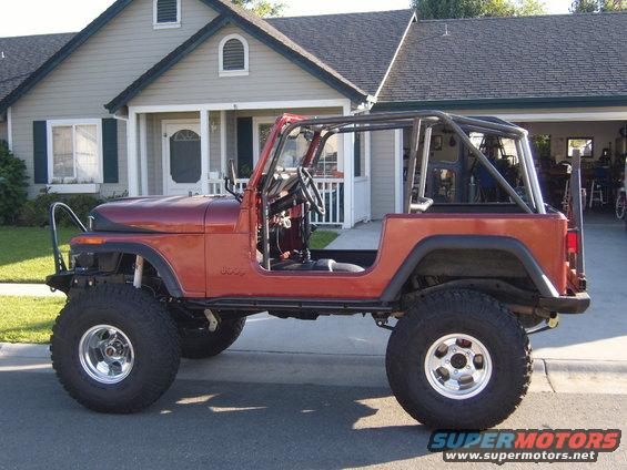 1985 Jeep CJ7 side profile, red body, roll cage, large tires, parked in driveway