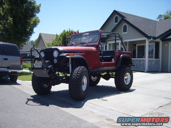 Red Jeep CJ7 with roll cage and large tires, parked in driveway