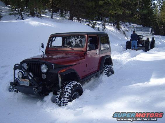 1985 Jeep CJ7 and another Jeep driving through deep snow on a wooded trail