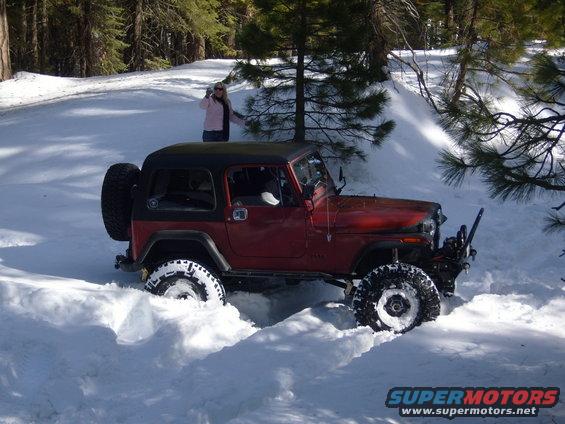 Red 1985 Jeep CJ7 with a black hardtop driving through deep snow, a woman stands in the background
