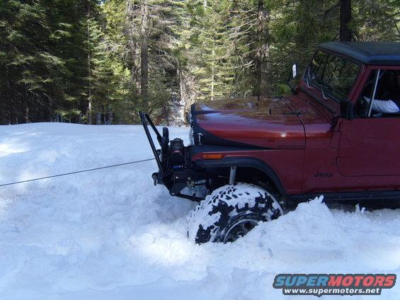 Red Jeep stuck in deep snow, winch cable attached to front bumper