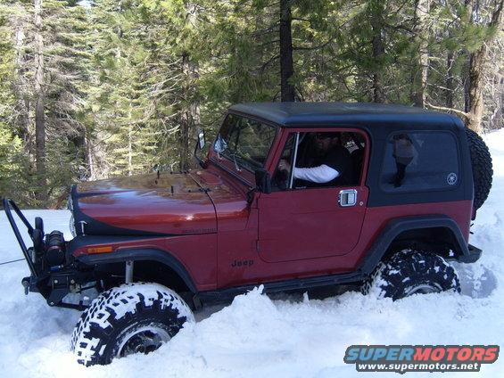 Red Jeep CJ-series stuck in snow, front winch visible, black hardtop