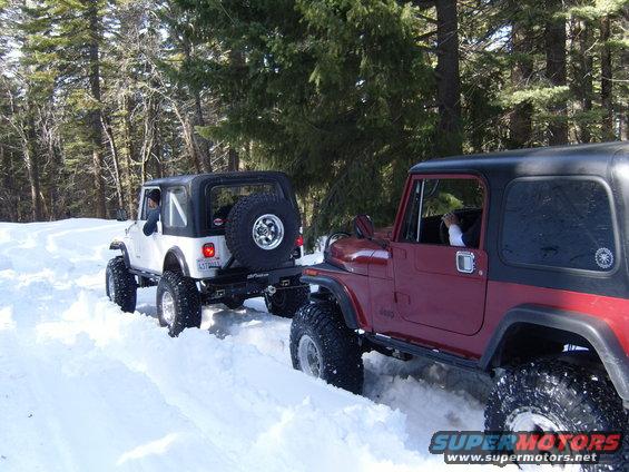 Two Jeep CJ-series vehicles navigate a snowy forest road