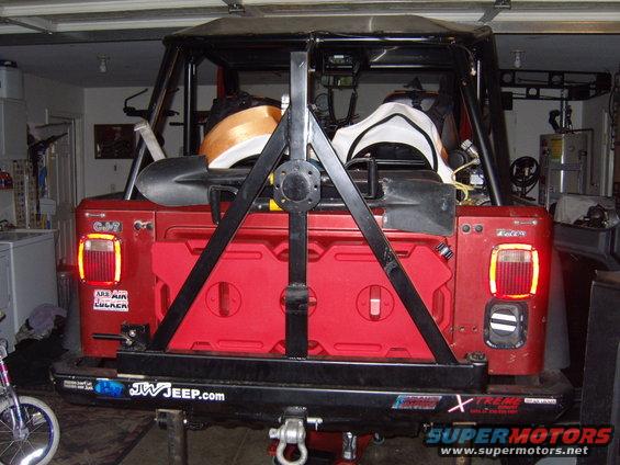 Red 1985 Jeep CJ7 rear view with spare tire carrier, jerry cans, and shovels