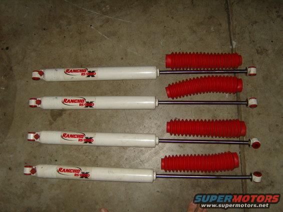 Four white Rancho RS9000 shock absorbers with red bellows laid out on a concrete surface