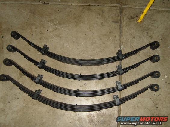 Four leaf springs laid out on a concrete floor. Supermotors.net logo visible