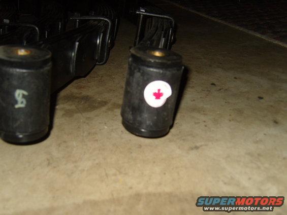 close up of two black leaf spring bushings, one has a white circle with a red maple leaf emblem